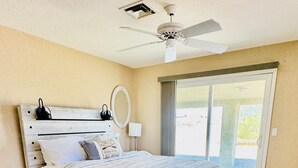 A bedroom with a wooden bed, a ceiling fan, a window with a view, and a door leading outside.