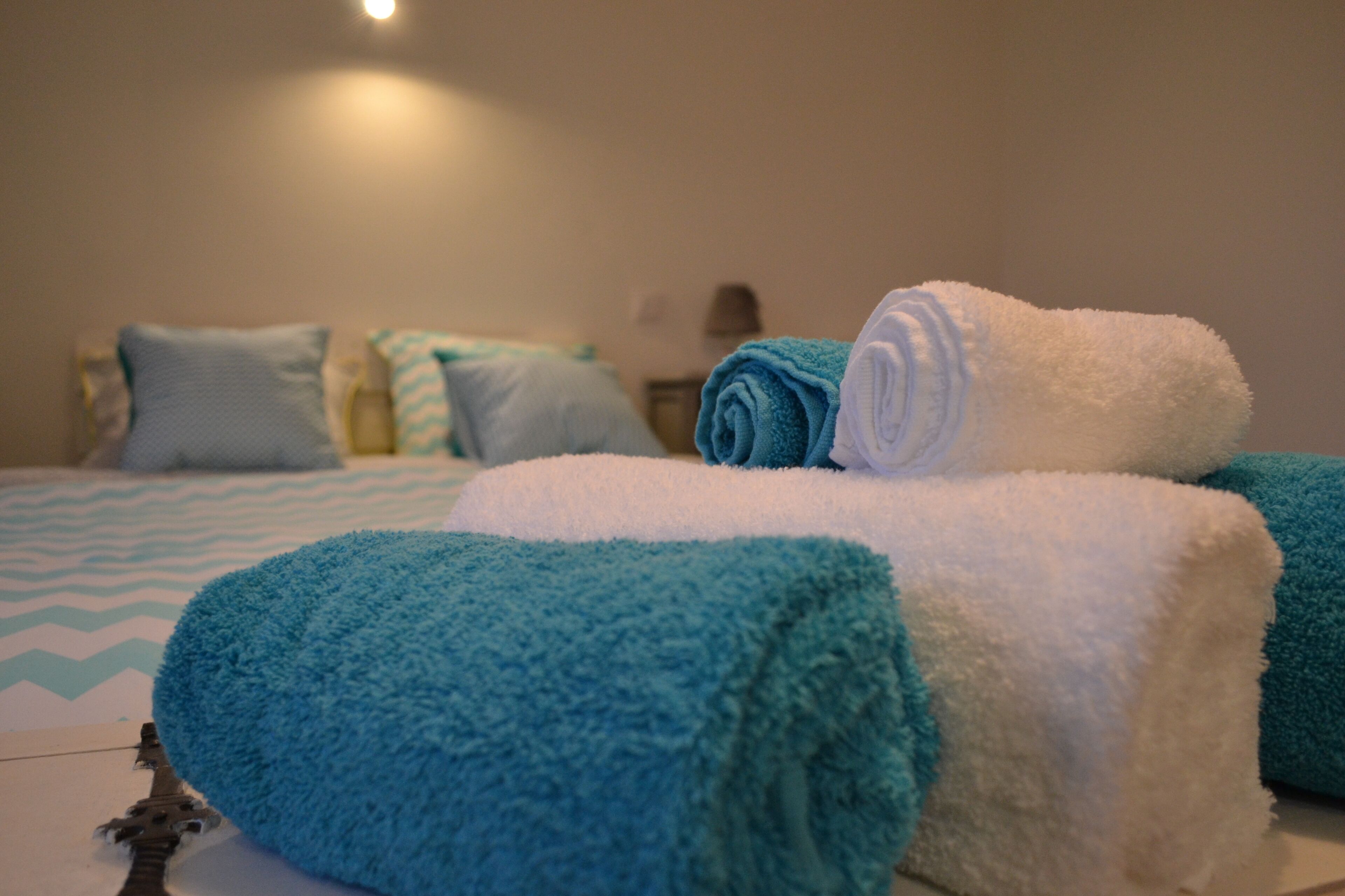 Una cama bien hecha con toallas azules y blancas, un edredón estampado y una lámpara fijada a la pared.