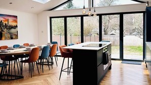 A modern kitchen with a central island, large windows, and a dining area with colorful chairs. - Best house on the street! Up to 10 guests- perfect for families, contractors (Coulsdon)