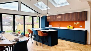 A modern kitchen with a central island, dark blue cabinets, and a bright orange accent wall. - Best house on the street! Up to 10 guests- perfect for families, contractors (Coulsdon)