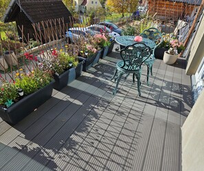 A rooftop garden with a metal table and chairs, surrounded by potted plants and flowers. - Sunny room 2 with own living room, bathroom, terrace (Dürrwangen)