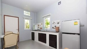 A kitchen with a white refrigerator, a dining table with chairs, and a window with a view of greenery. - 2bdr BangTao House (Choeng Thale)
