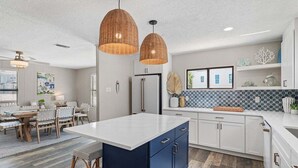 Une cuisine moderne dotée d’un grand îlot central, de luminaires suspendus et d’un dosseret carrelé.