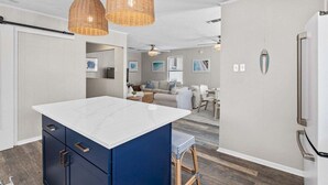 Une cuisine moderne avec un îlot central blanc, des armoires bleues et des suspensions en osier.