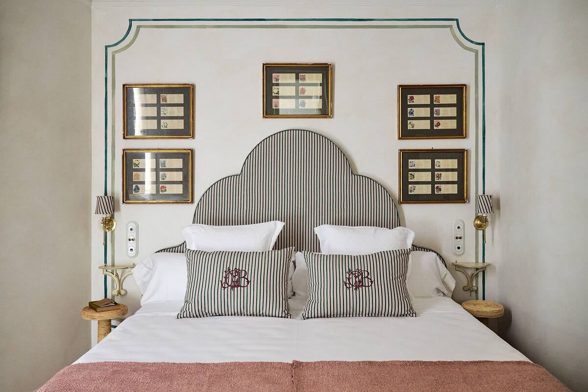 A neatly made bed with striped pillows and a headboard, flanked by framed documents on the wall.