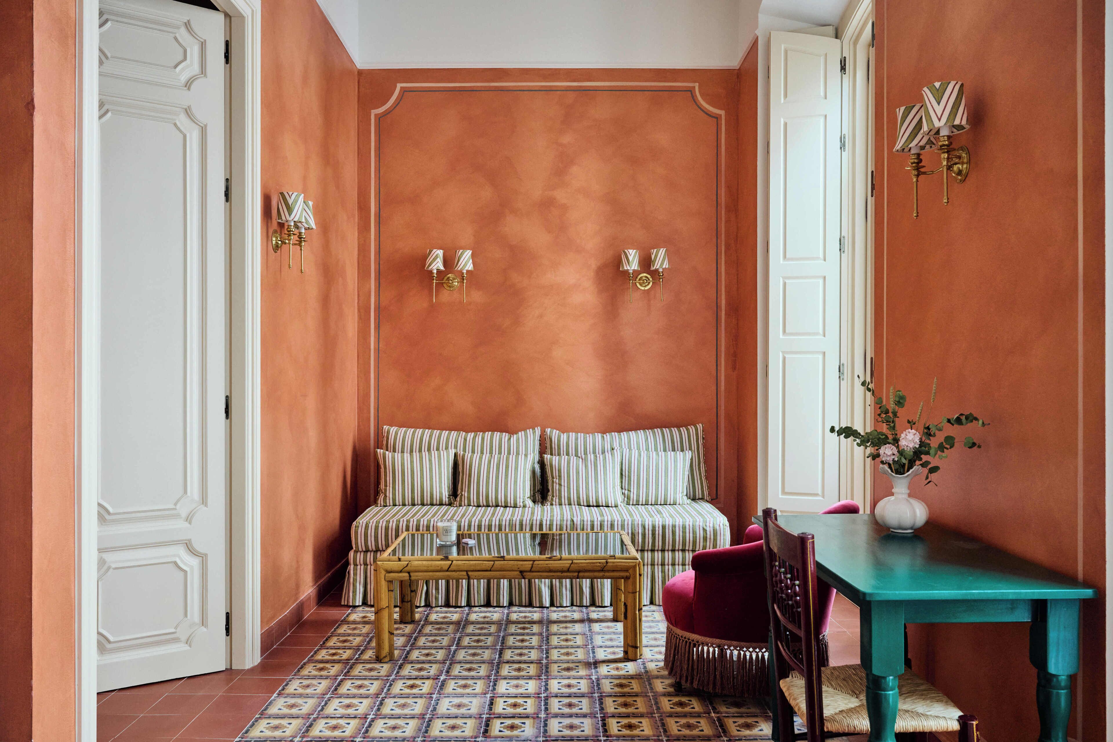 Ein Zimmer mit einem gemusterten Boden, einem gestreiften Sofa, einem Holztisch, einem Türkistisch und einer Vase mit Blumen.