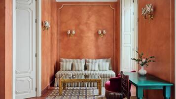 Ein Zimmer mit einem gemusterten Boden, einem gestreiften Sofa, einem Holztisch, einem Türkistisch und einer Vase mit Blumen.
