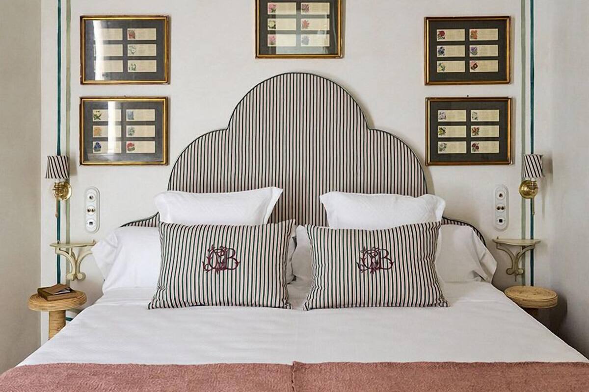 A bed with striped bedding, a large headboard, and framed artwork on the walls.