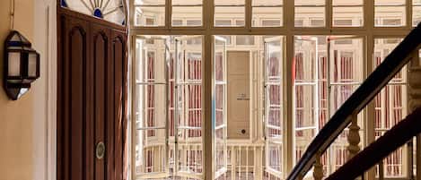 Una escalera con barandilla de madera y vistas a una habitación con ventanas abiertas y una puerta con pomo de latón.