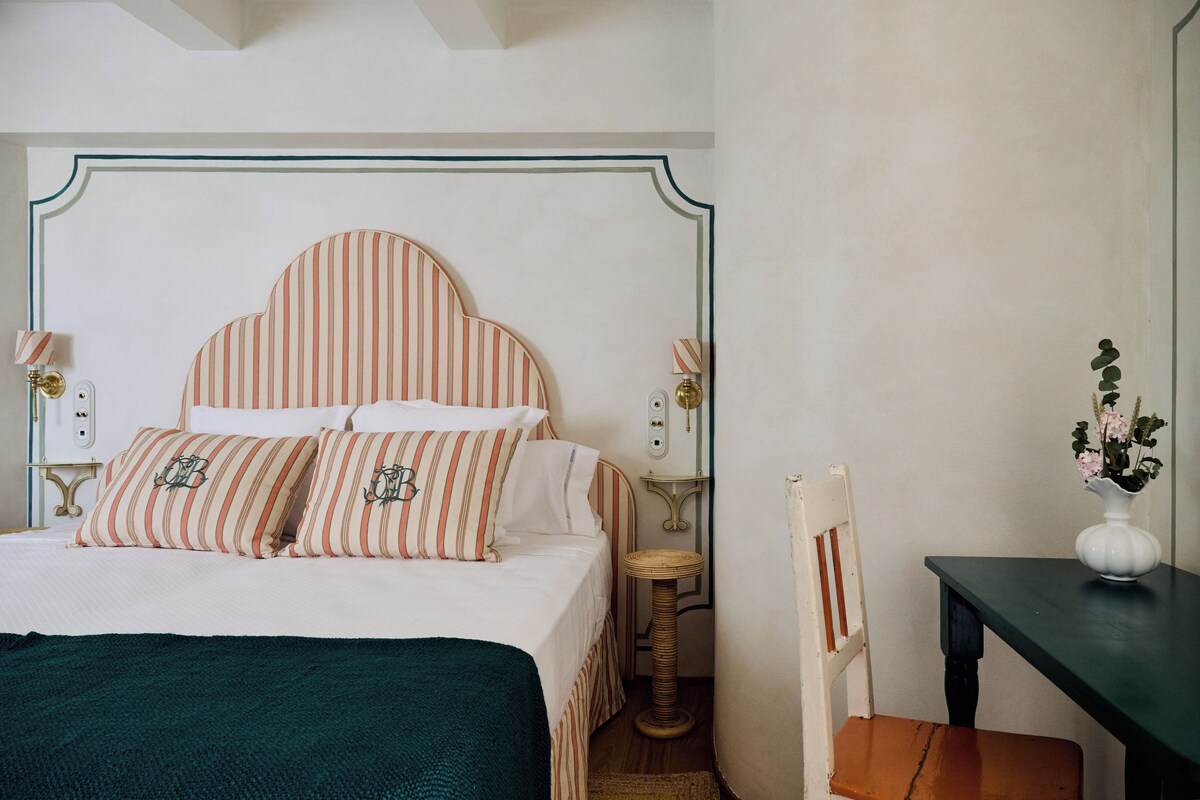 Ein ordentlich eingerichtetes Schlafzimmer mit einem Bett, Nachttischen, einem Sessel und einem kleinen Tisch mit einer Vase.