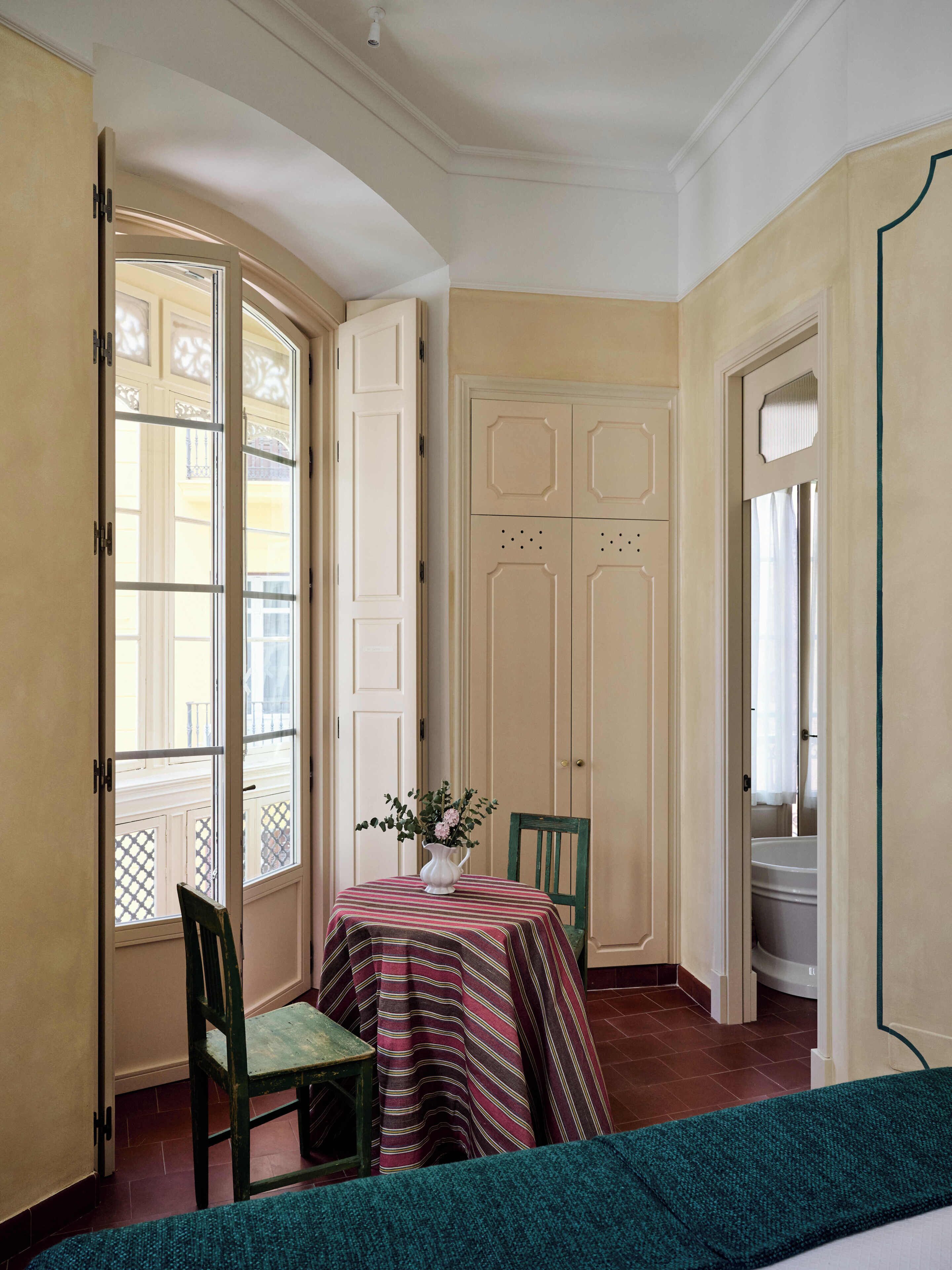 Una stanza con un tavolo da pranzo, sedie, un vaso con fiori e vista dalla finestra.