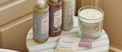 A small round table with a white and blue striped design, holding various toiletries including body wash, shampoo, and a candle labeled "Cristine Bedfor".