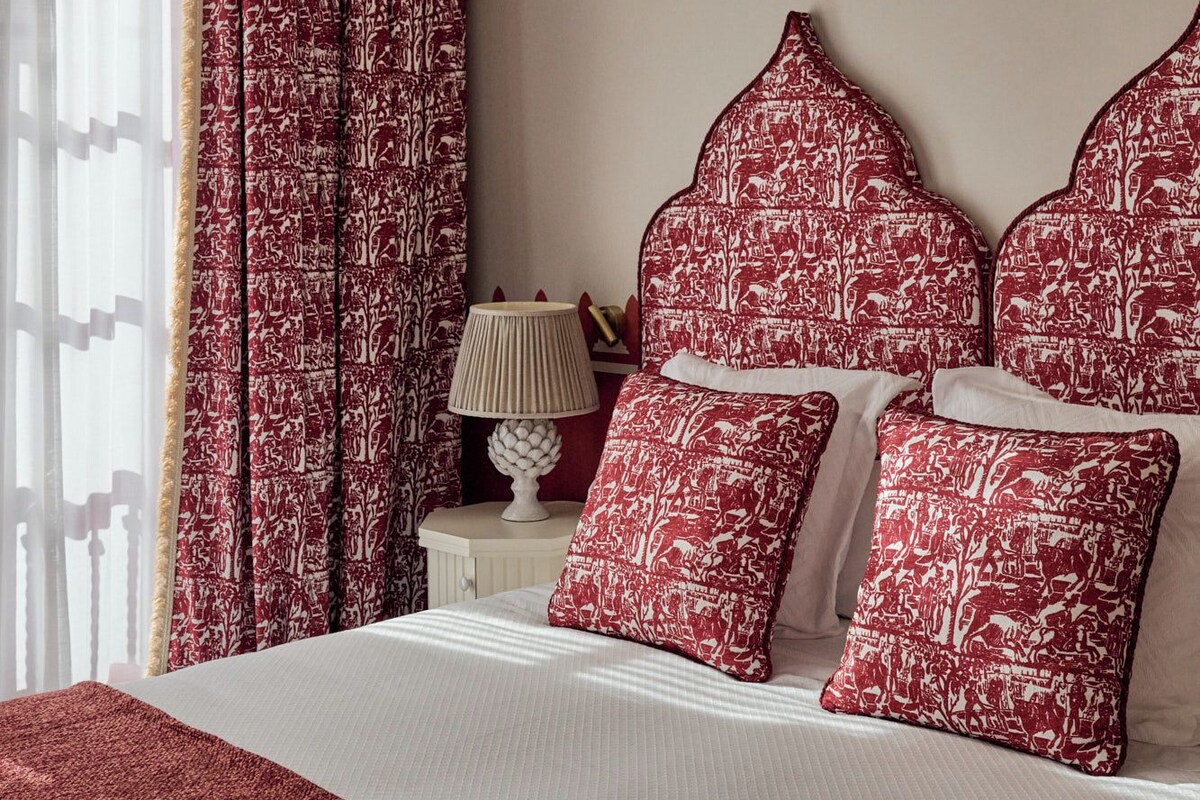 A bedroom with a bed, red patterned pillows, a star-shaped hanging light, and a nightstand with a lamp.