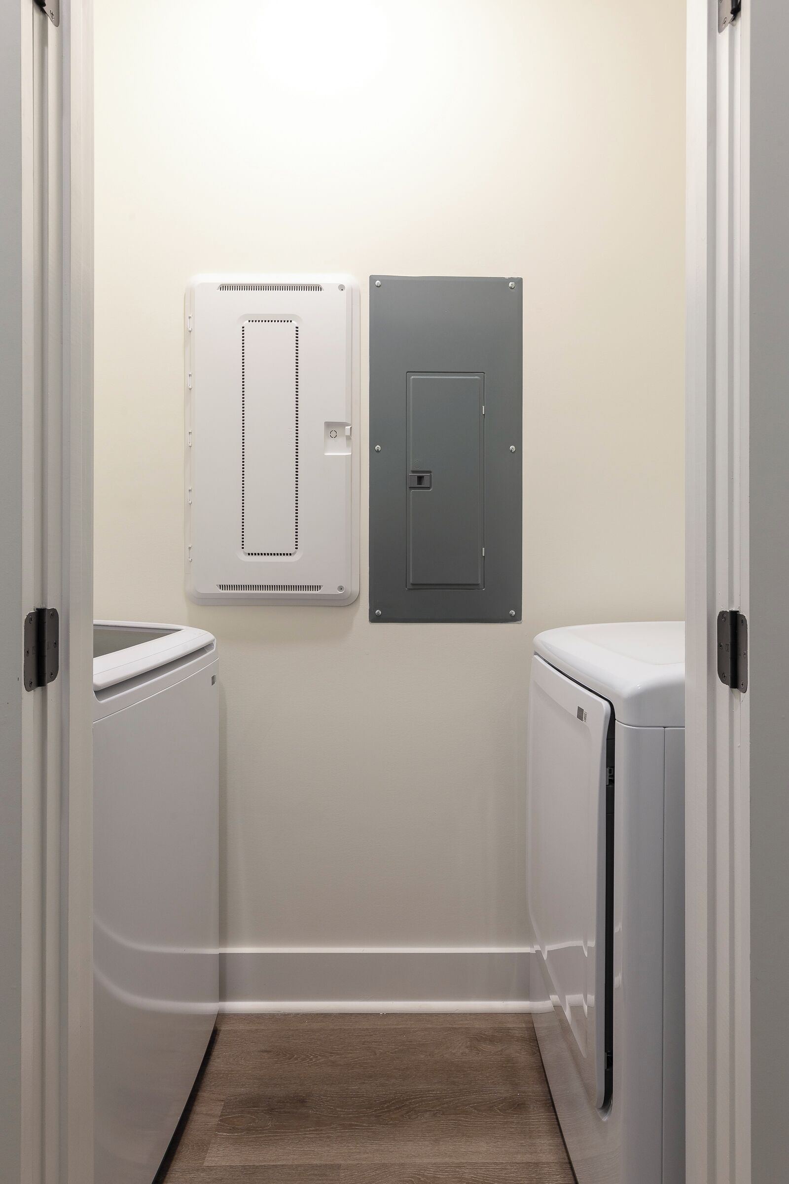 Une buanderie équipée de deux machines à laver blanches, d’un coffret électrique gris et d’un tableau électrique blanc fixé au mur.