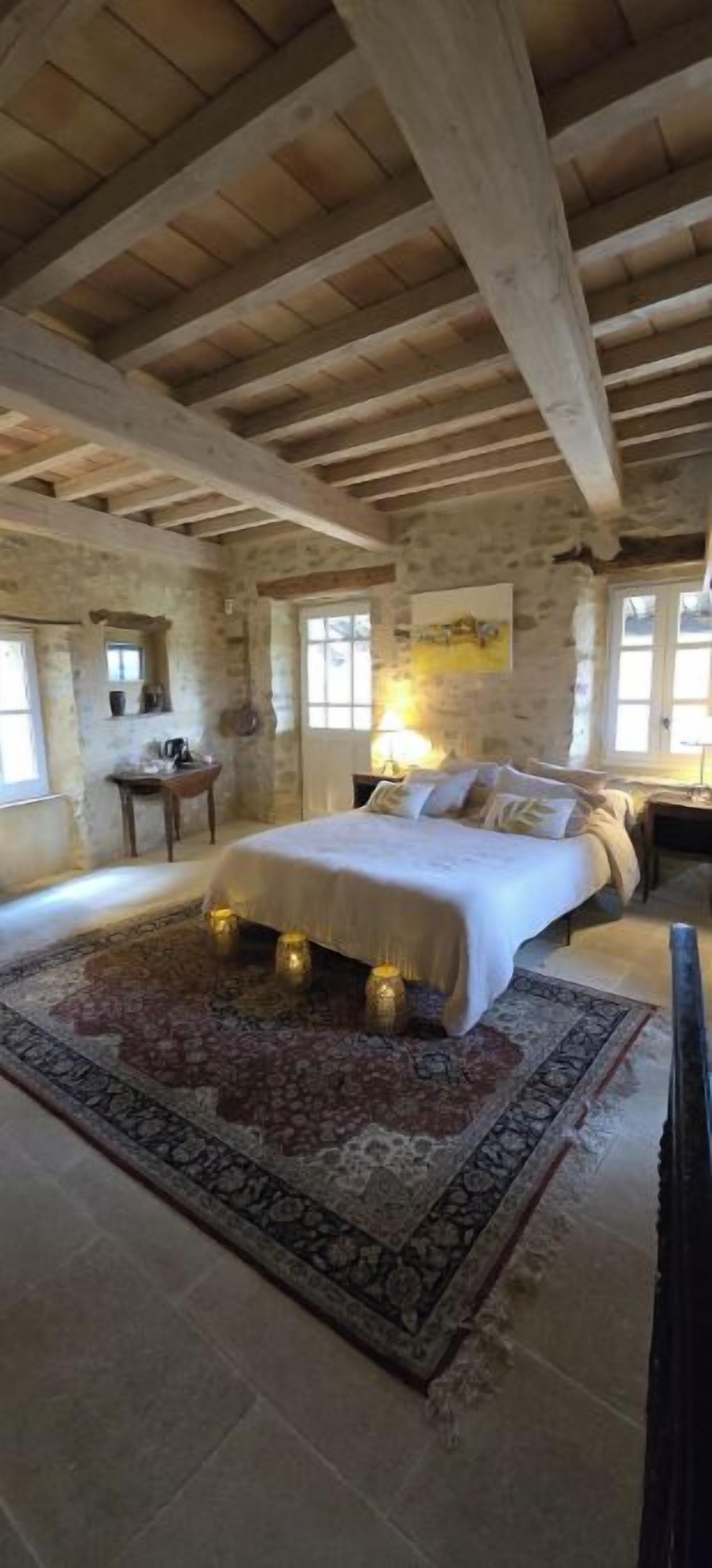 Une chambre avec un grand lit, un mur en pierre, un plafond en bois et une fenêtre.