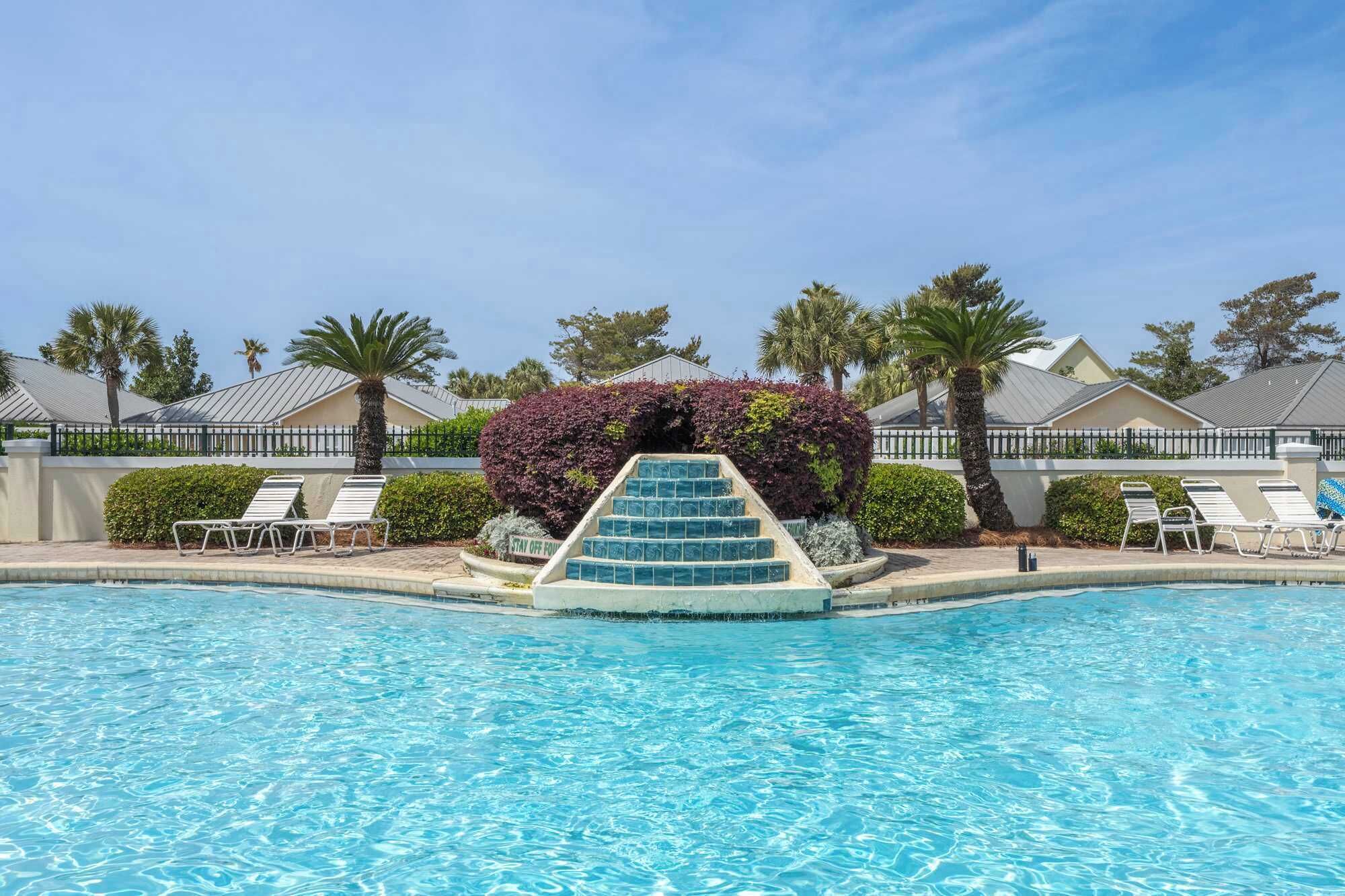 A swimming pool with a set of stairs leading into it, surrounded by lounge chairs and palm trees.