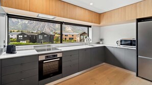 A modern kitchen with a large window, built-in appliances, and a view of houses and mountains.
