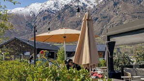 An outdoor seating area with umbrellas, a view of snow-capped mountains, and a building with a sloped roof.