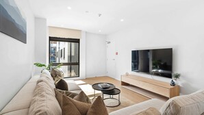 A modern living room with a sofa, coffee table, TV, and a window with a view of buildings.