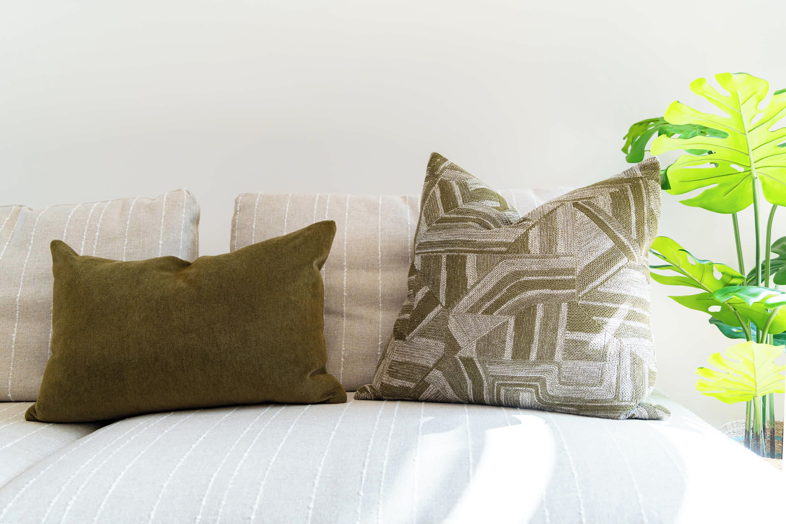 A bed with striped bedding, two pillows, and a green plant in a vase.