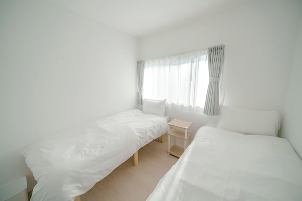 A room with two single beds, a small bedside table, and a window with curtains. - TRANSIT HOSTEL (Izumisano)