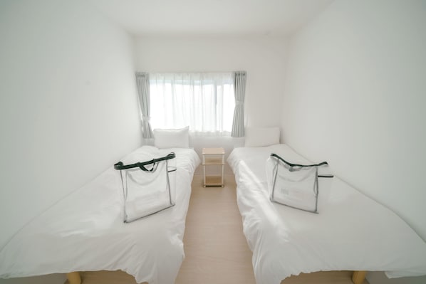 Une petite chambre propre, avec deux lits simples, une petite table et une fenêtre avec des rideaux.
