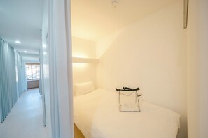 A hotel room with a neatly made bed, a bedside table with a bag, and a window with curtains. - TRANSIT HOSTEL (Izumisano)