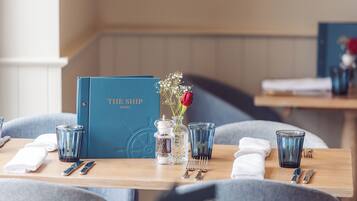 A dining table with a menu titled "THE SHIP HOTEL," a vase with flowers, and cutlery.