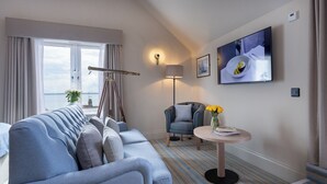A modern hotel room with a sofa, a chair, a small table with flowers, a lamp, and a TV on the wall. - The Ship Hotel (Leigh-on-Sea)