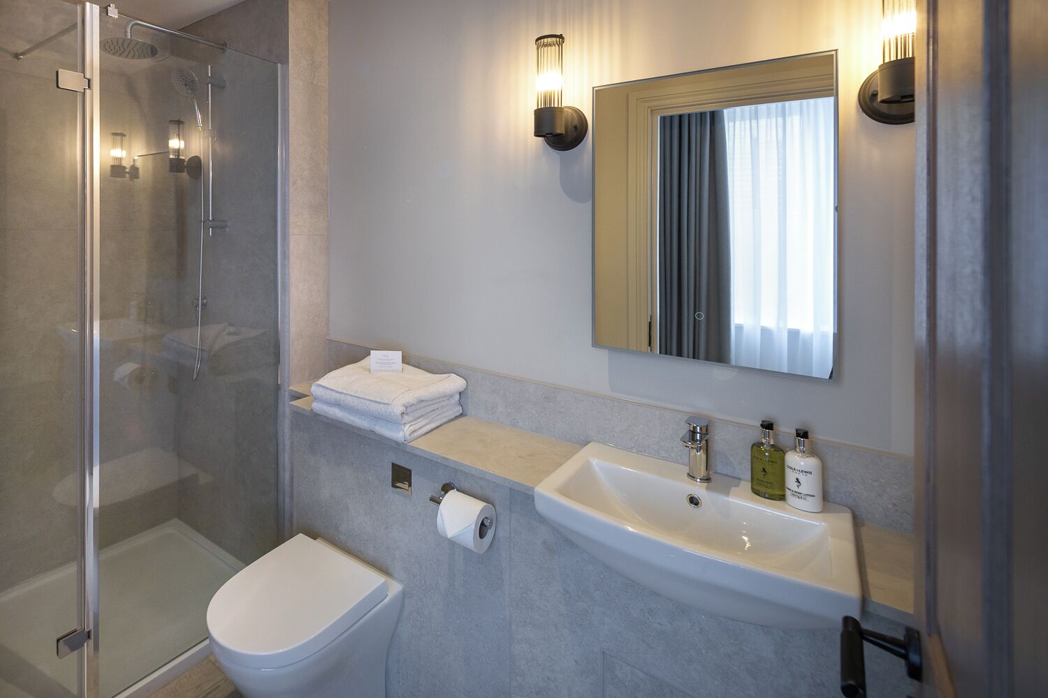 A modern bathroom with a glass shower enclosure, a white toilet, a sink with a mirror above it, and a towel rack.