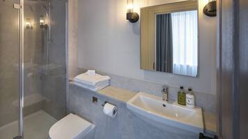 A modern bathroom with a glass shower enclosure, a white toilet, a sink with a mirror above it, and a towel rack.