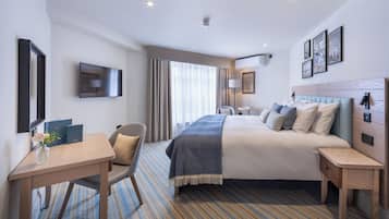 Une chambre d’hôtel avec un grand lit, un bureau, une chaise, une télévision et une fenêtre avec des rideaux.