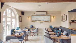 A restaurant with a nautical theme, featuring a large painting of a seascape, wooden beams on the ceiling, and a mix of table and booth seating. - The Ship Hotel (Leigh-on-Sea)