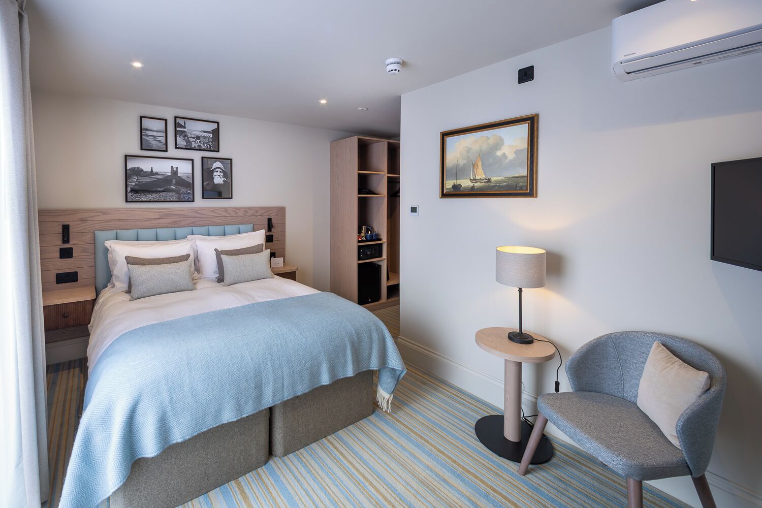 A hotel room with a bed, a chair, a lamp, a TV, and a painting on the wall.