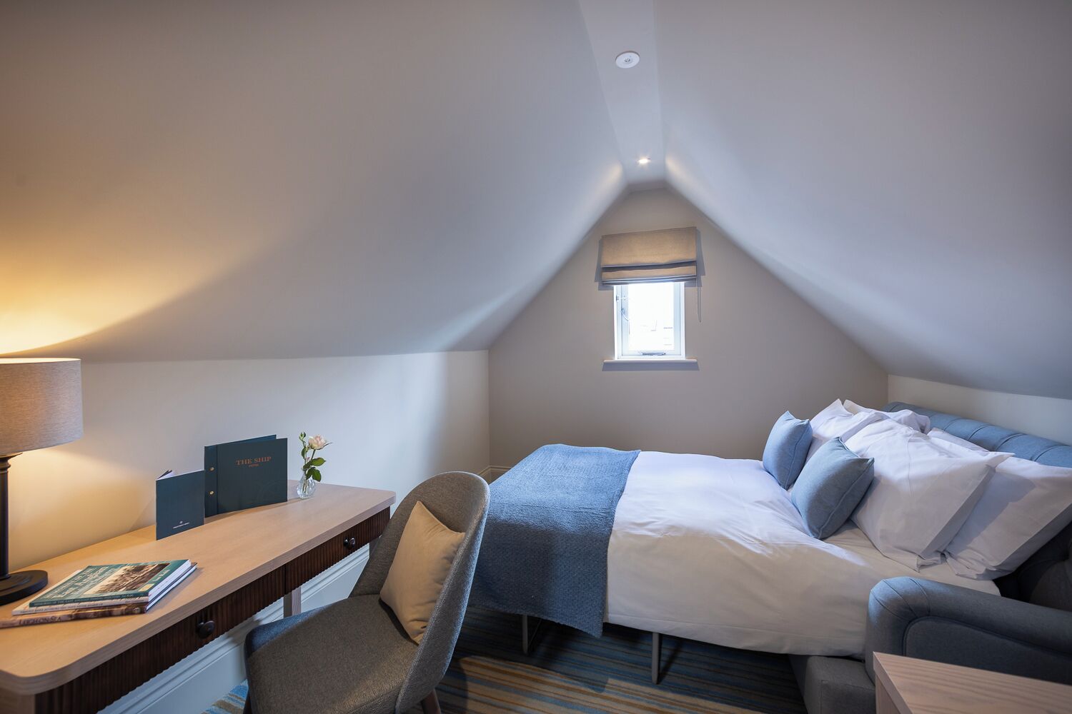 Une chambre à coucher avec un lit, un bureau, une chaise, une fenêtre et une lampe.