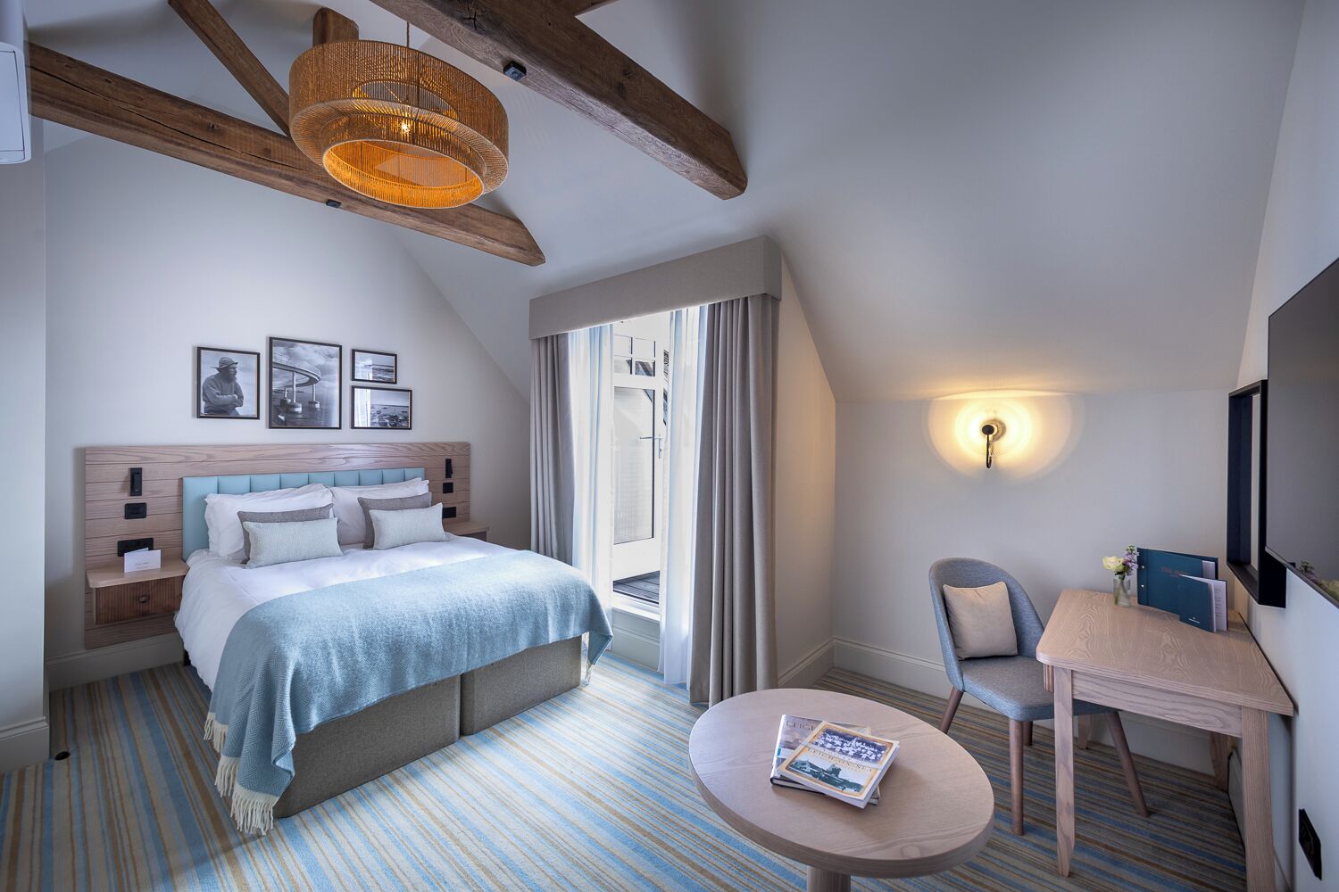 A modern hotel room with a large bed, a small round table, a chair, and a large window.