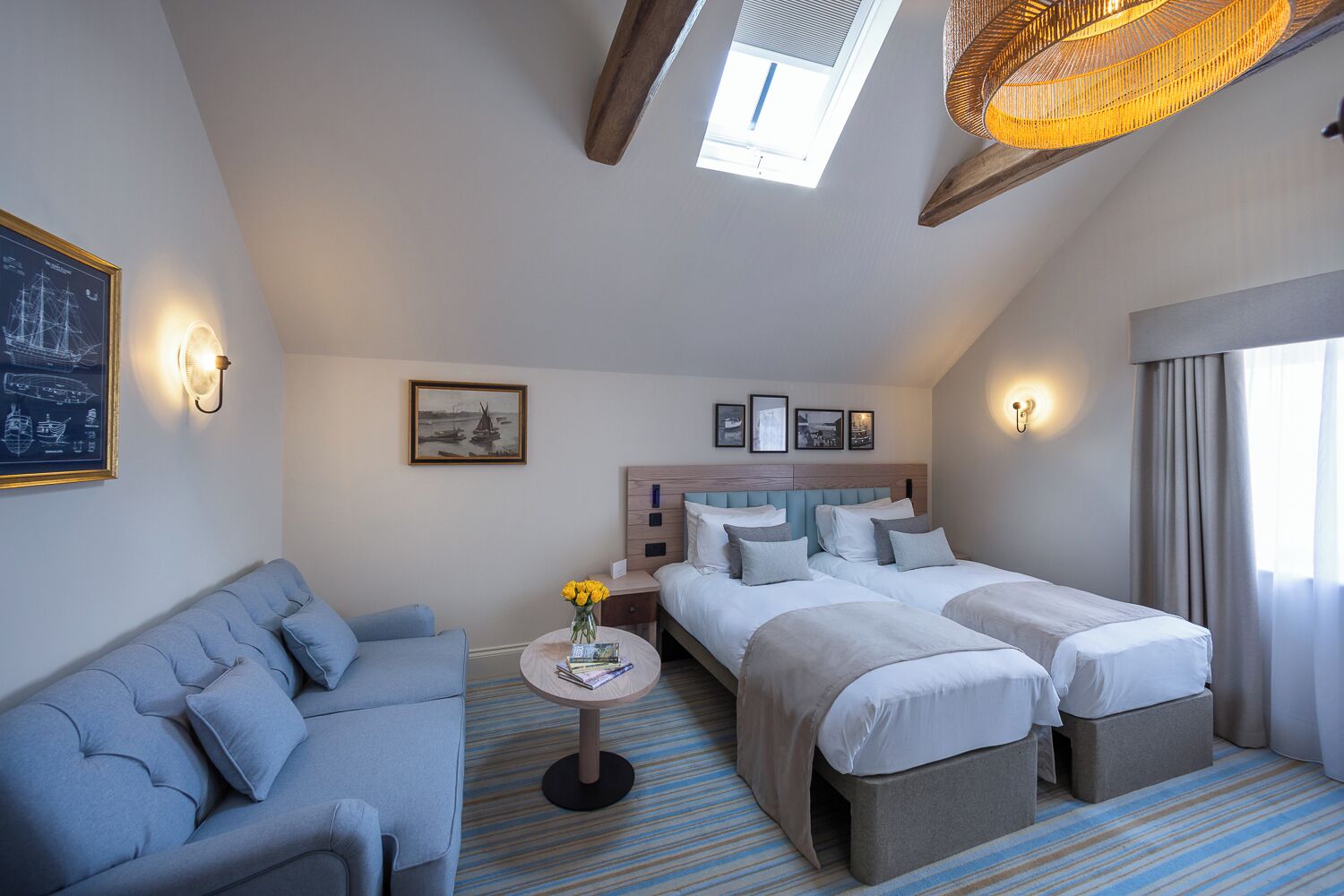 A hotel room with a bed, a sofa, a small table with flowers, and artwork on the walls.