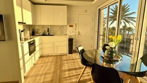 A modern kitchen with white cabinets, a dining area with a glass table and black chairs, and a ceiling fan.