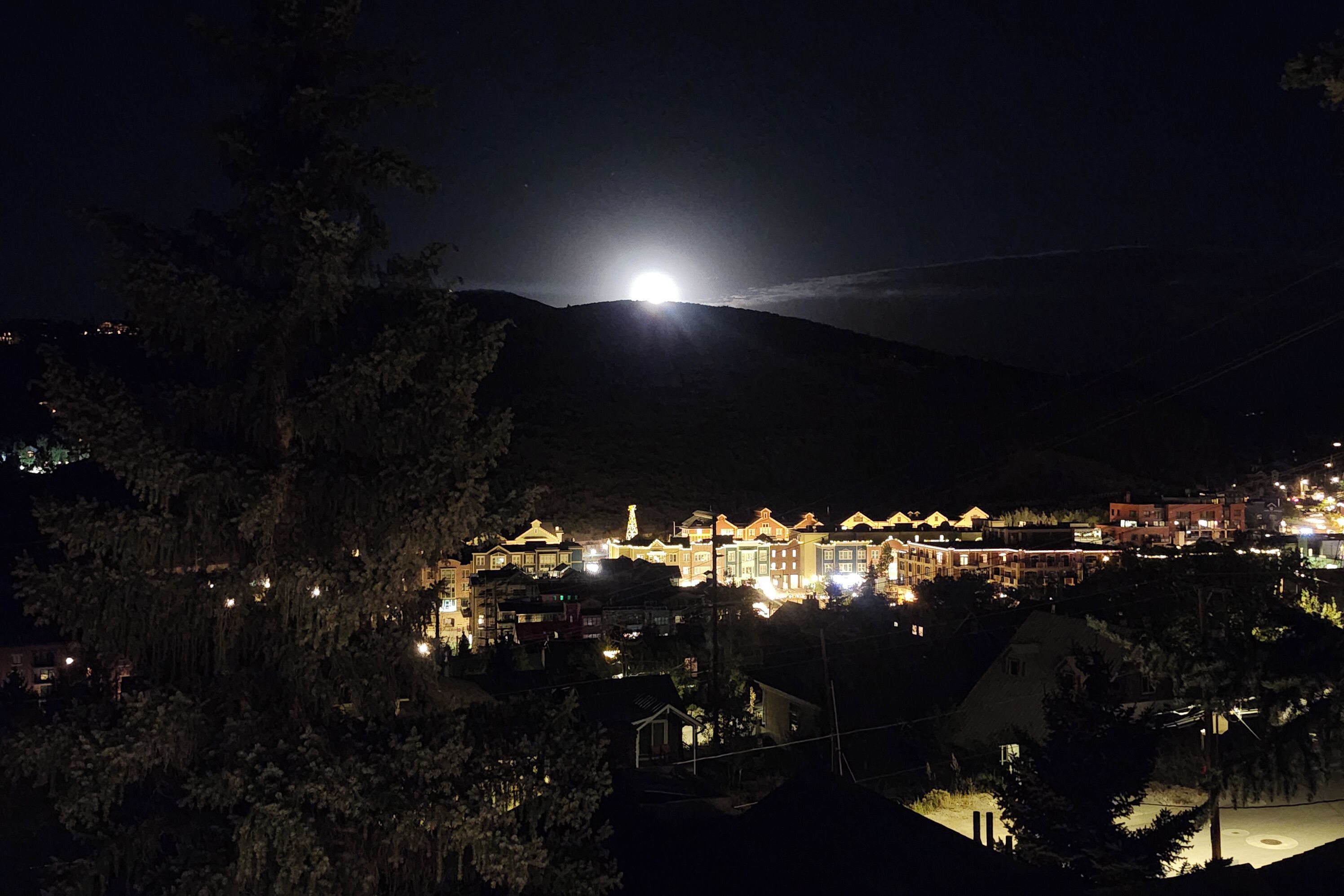 A nighttime view of a mountain town with illuminated buildings and a bright moon in the sky.