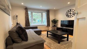 A living room with a sofa, a coffee table, a TV, and a clock on the wall.