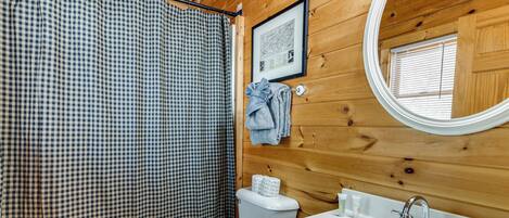 Baño de cabaña de madera con cortina de ducha a cuadros, un inodoro, un lavabo con espejo y un mapa enmarcado en la pared.