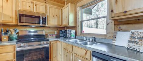 A modern kitchen with wooden cabinets, stainless steel appliances, and a large window providing a view of the outdoors.