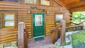Une cabane en rondins avec une porte verte, des marches en bois et une rambarde en bois.