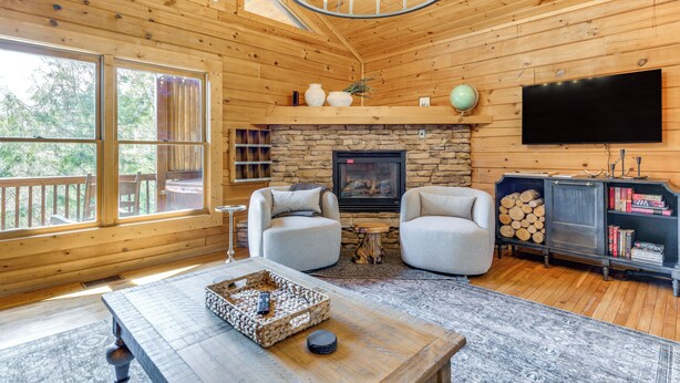 L’intérieur d’un chalet accueillant, avec une cheminée en pierre, deux fauteuils, une table basse et un téléviseur fixé au mur.