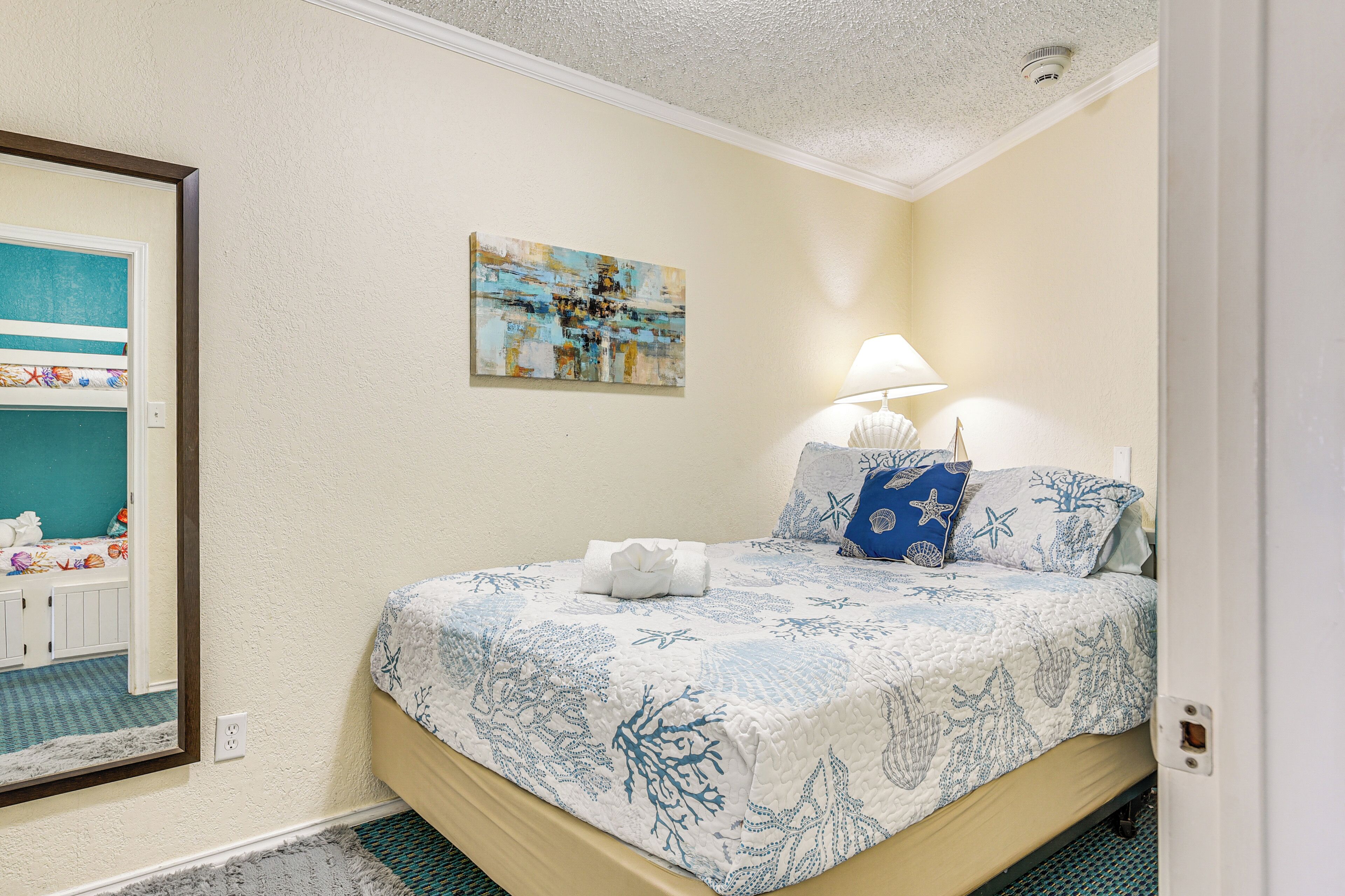 A bedroom with a bed, a painting, and a nightstand with a lamp.