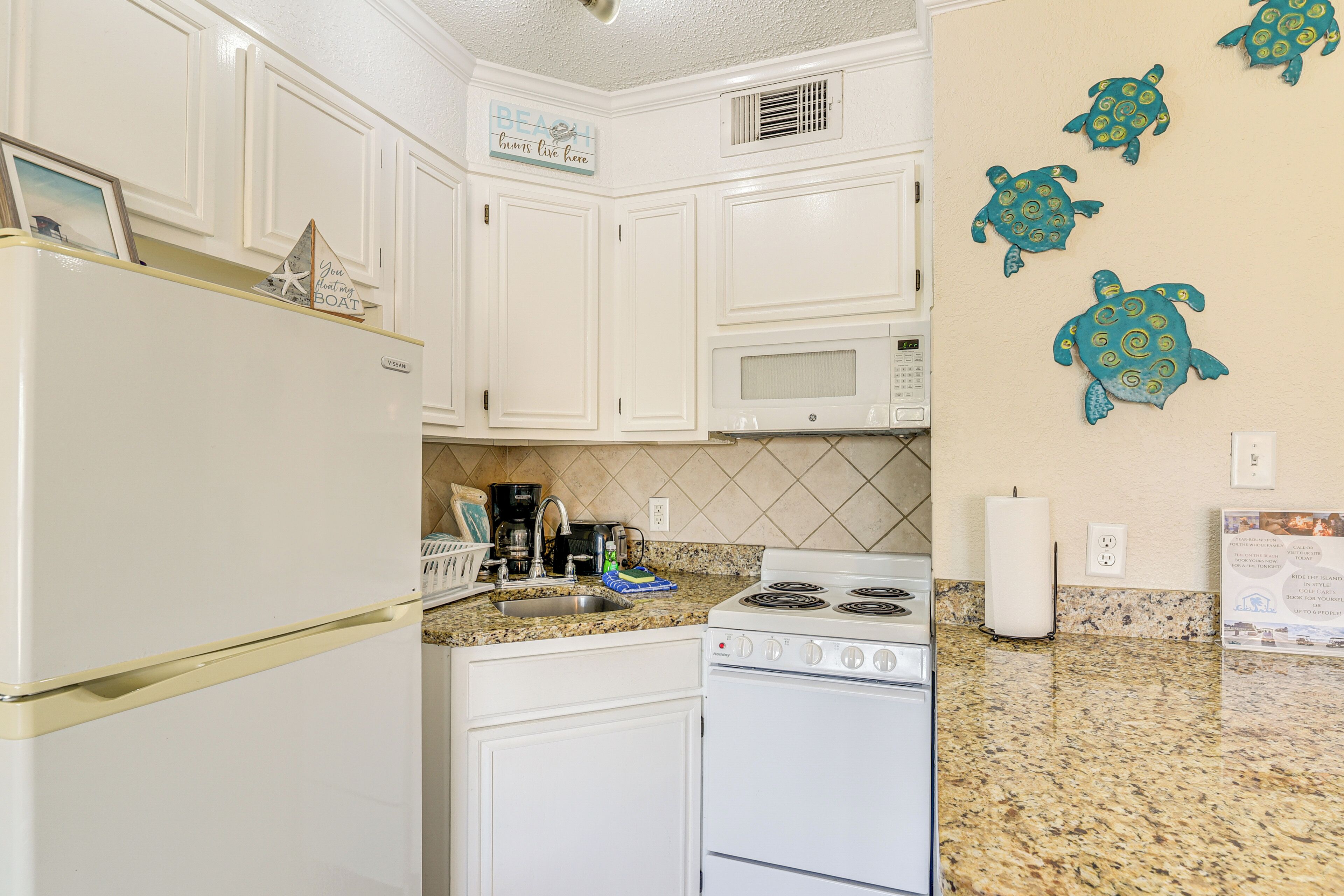A kitchen with white cabinets, a stove, a microwave, and a granite countertop.