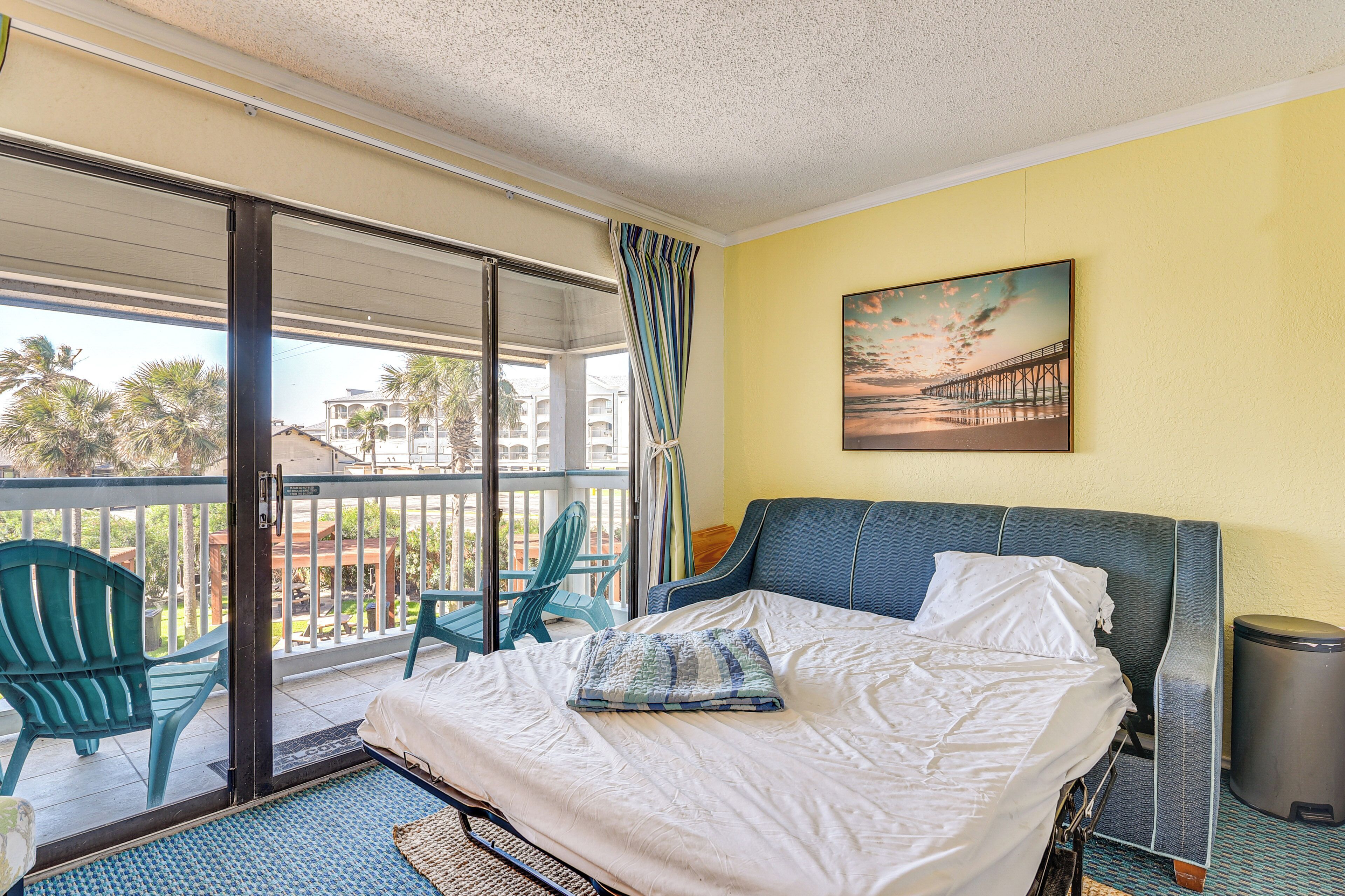 Ein Hotelzimmer mit Bett, Balkon mit Sitzgelegenheiten, einem Wandbild und einem Mülleimer.