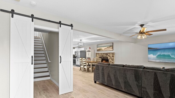 A modern living room with a gray sofa, a dining area with a table and chairs, and a staircase leading to another level.
