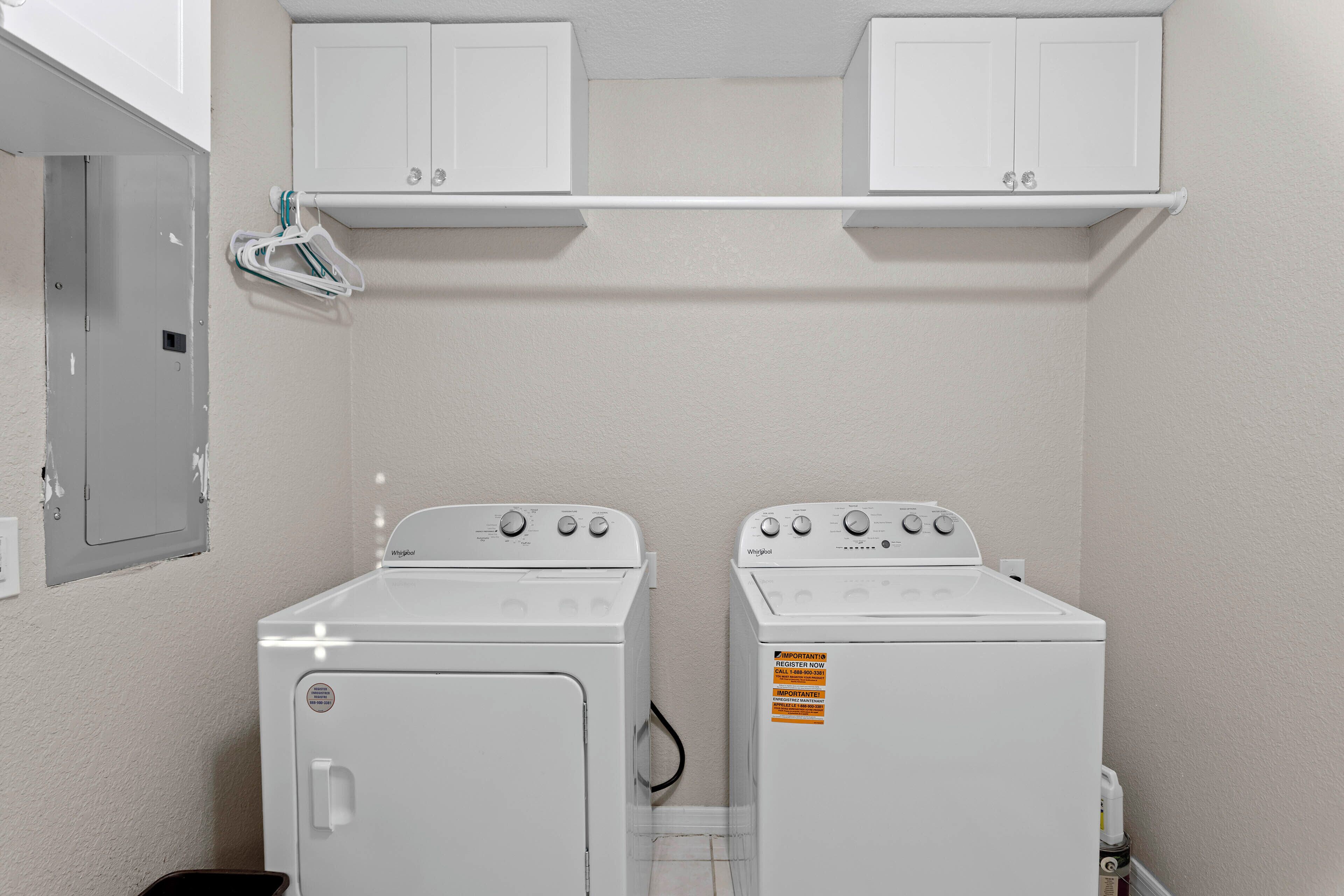 A laundry room with two white Whirlpool washers and dryers, a white wall, and a metal utility door.
