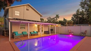 A backyard with a swimming pool, covered patio area with seating, and a house.